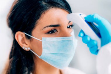 Coronavirus. Tehlikeli madde koruma süitinde çalışan sağlık görevlisi vücut ısısını kontrol ediyor, koruyucu maskeli kadın.