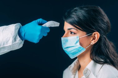 Coronavirus. Tehlikeli madde koruma süitinde çalışan sağlık görevlisi vücut ısısını kontrol ediyor, koruyucu maskeli kadın.