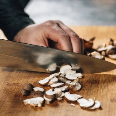 Şitake mantarlarını tahta kesme tahtasına bıçakla kesen şef.