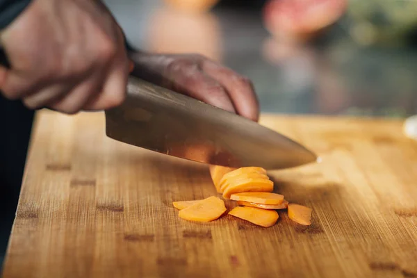 Preparing a Vegan Meal. Chef cutting carrots on a wooden cutting board, close-up