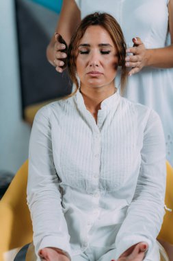 Shamballa Terapisti kadın müşterinin başının üstünde el ele tutuşuyor. Şemsiye Tedavisi