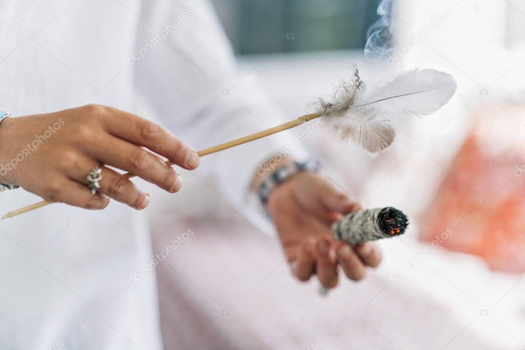 Womans hand holding bundle of dried sage herb, performing smudging ritual, cleansing negative energy and purifying living space with smoke 