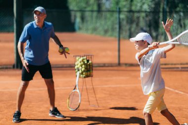 Kil kortunda Tenis Dersi Veren Çocukla Tenis Eğitmeni.