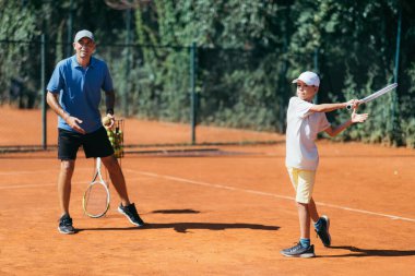 Kil kortunda Tenis Dersi Veren Çocukla Tenis Eğitmeni.