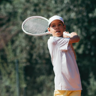 Çocuk dışarıda tenis oynuyor. 