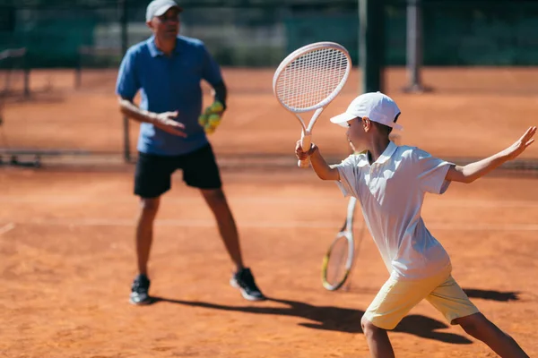 男孩在泥场上有网球课的网球教练 — 图库照片