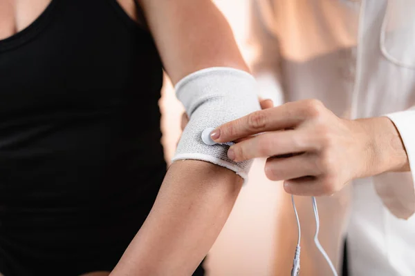 Elbow Physical Therapy with TENS Electrode Brace Pads, Transcutaneous Electrical Nerve Stimulation. Therapist Positioning Electrodes onto Patient's Elbow