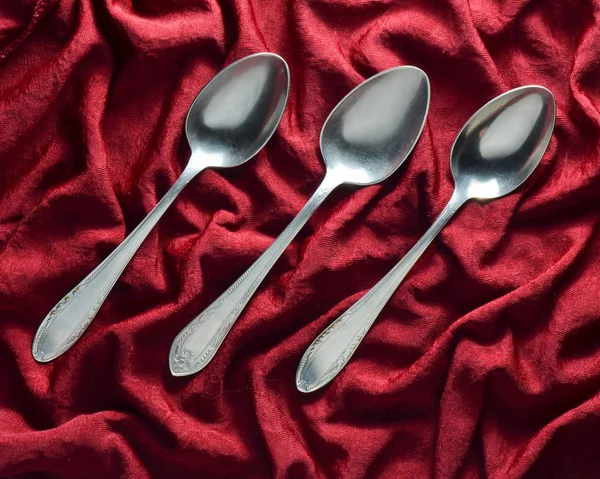 A set of three metal spoons on a red silk tablecloth. Top view. — Stock Photo, Image