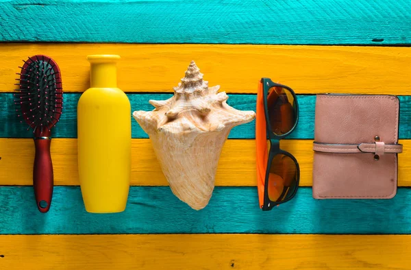 Trend příslušenství pro relaxaci na pláži a krásy na žluté modré dřevěný stůl. Kabelka, hřeben, sluneční brýle, shell, opalovací krém. Koncept resort na pláži. — Stock fotografie