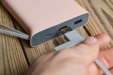 Bir el ahşap arka plan üzerinde bir güç banka a usb tel kablo bağlanır. Harici pil.
