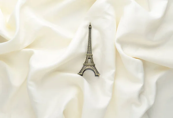 Miniatyr statyett av Eiffeltornet på vit silk bakgrund. Trenden minimalism Souvenir från Paris. Ovanifrån. — Stockfoto