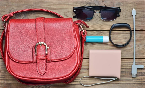 Red leather bag and other female accessories layout on a wooden desk. Top view. Trend of minimalism. Flat lay.