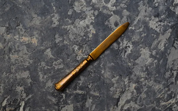 An antique gold-plated knife on a concrete surface. Top view.