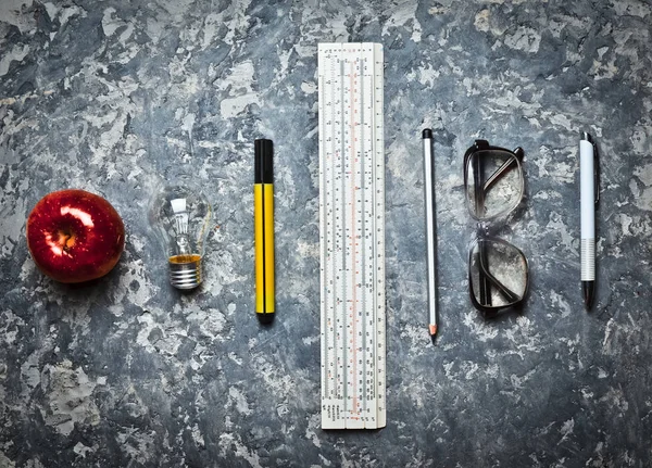 Stationery tools for the education of engineering students. Workspace on a concrete background. I have an idea! Ruler, marker, pencil, pen, glasses, apple, incandescent bulb. Top view. Flat lay.