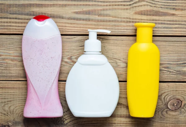 Garrafas de produtos para o banheiro. Gel de chuva, sabão líquido, xampu em uma mesa de madeira. Vista superior . — Fotografia de Stock