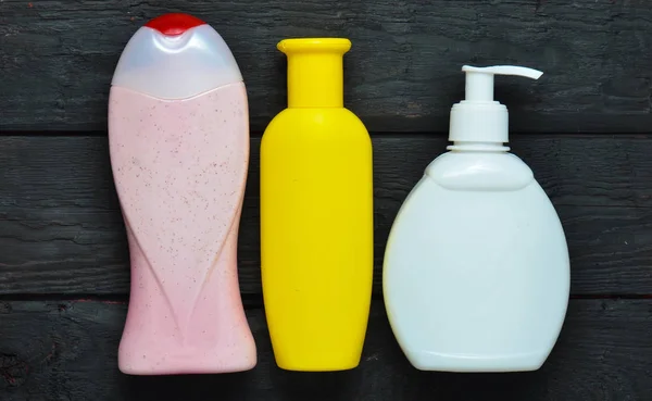 Botellas de productos para ducha. Gel de ducha, jabón líquido, champú sobre una mesa de madera negra. Vista superior . —  Fotos de Stock