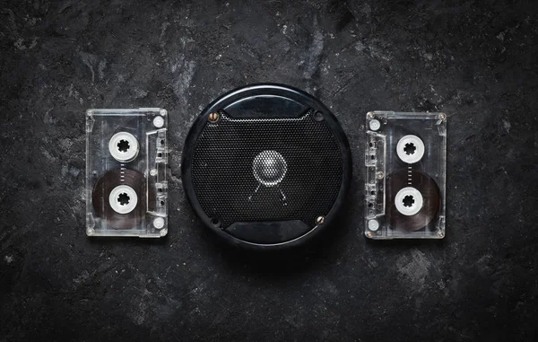 Acoustic speaker and audio cassette on a black concrete table. Retro technology. Meloman. Top view. Flat lay.