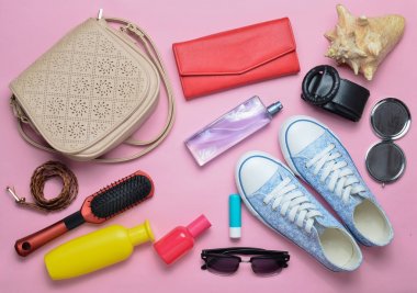 Kadınların çantada ne var? Bir geziye gidiyor. Girly şık bahar ve yaz aksesuarları: spor ayakkabı, kozmetik, güzellik ve hijyen ürünleri, bir çanta, pastel pembe bir arka plan üzerinde güneş gözlüğü. Üstten Görünüm.