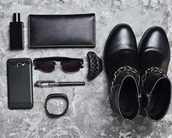 Bottes, accessoires, gadgets pour femme d'affaires sur une surface en béton. Flacon de parfum, sac à main, stylo, smartphone, bracelet intelligent, lunettes de soleil. Couleurs gris noir. Tendance à plat. Vue du dessus . — Photo