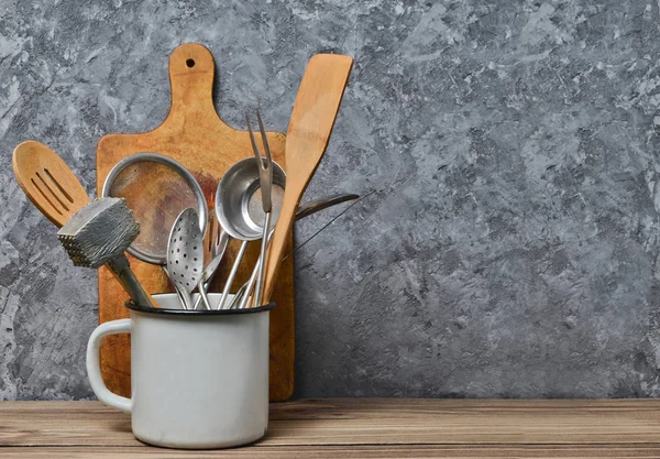 Ferramentas de cozinha para cozinhar em uma mesa de madeira no fundo de uma parede de concreto. Colheres, garfos, espátula de madeira . — Fotografia de Stock