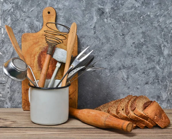 Cocina casera, panadería. Tablero de madera, herramienta de cocina, pan de centeno en una mesa en el fondo de una pared de hormigón gris . — Foto de Stock