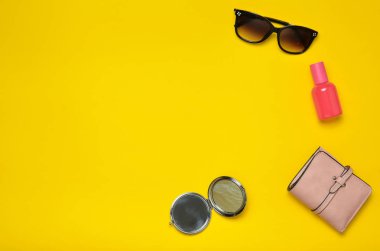 Sarı bir arka plan üzerinde izole kadın aksesuarları. Güzellik ve moda için ürünler. Güneş gözlüğü, bir çanta, parfüm şişe, bir ayna. Üstten Görünüm. Uzay kopyalayın. Düz yatıyordu.