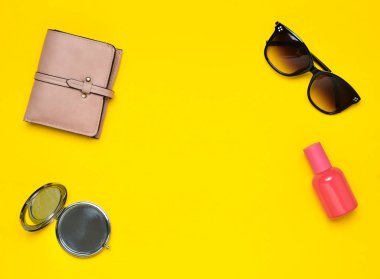 Sarı bir arka plan üzerinde izole kadın aksesuarları. Güzellik ve moda için ürünler. Güneş gözlüğü, bir çanta, parfüm şişe, bir ayna. Üstten Görünüm. Uzay kopyalayın. Düz yatıyordu.