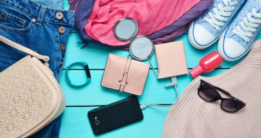 Kadın moda aksesuarları, Ayakkabı, giyim ve mavi ahşap arka plan üzerinde modern araçlar. Kot pantolon, çanta, Ayakkabı, smartphone, akıllı bilezik, güç banka, kozmetik, güneş gözlüğü, eşarp. Üstten Görünüm.