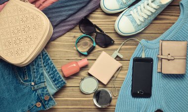 Kadın moda aksesuarları, Ayakkabı, giyim ve ahşap arka plan üzerinde modern araçlar. Kot pantolon, çanta, Ayakkabı, smartphone, akıllı bilezik, güç banka, kozmetik, güneş gözlüğü, eşarp. Üstten Görünüm. Düz yatıyordu.
