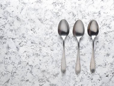 Beyaz beton yüzeyinde metal kaşık kümesi. Üstten Görünüm.