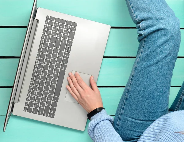 一个现代的女孩坐在蓝色的木地板上, 并使用笔记本电脑。世代 z。自由职业者的概念。工作空间。顶部视图. — 图库照片