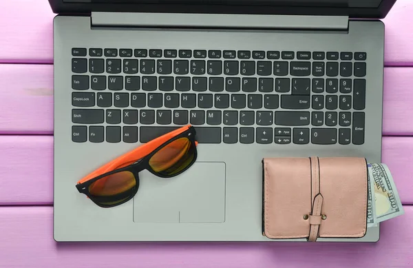 The concept of web work at a beach resort, freelancing. Laptop, sunglasses, purse on a violet color wooden table. Top view.