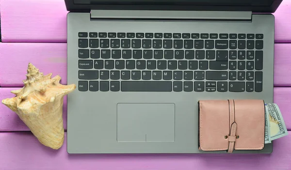 The concept of web work at a beach resort, freelancing. Laptop, shell, purse on a violet color wooden table. Top view.