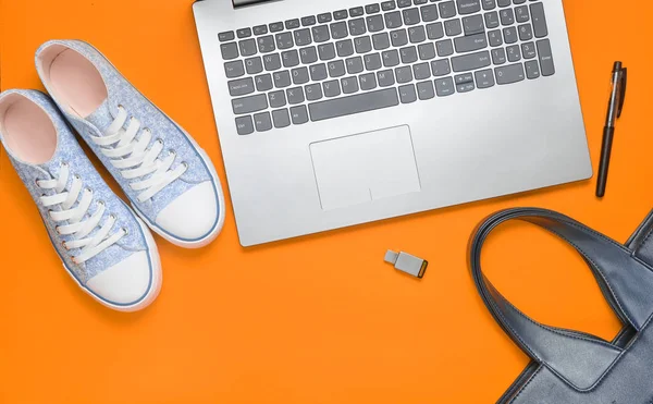 Digital technology and fashionable women's accessories on an orange background: laptop, usb flash drive, bag, sneakers, bag. Top view. Flat lay.