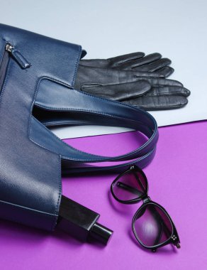 Deri çanta, güneş gözlüğü, eldivenler, gri-mor arka planda parfüm şişesi. Kadın moda aksesuarları
