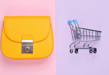 Alışverişkolik minimalist kavram. Sarı çanta, pastel arka planda mini alışveriş arabası. Üst görünüm