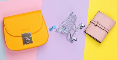 Alışverişkolik minimalist kavram. Çanta, çanta, pastel arka planda mini alışveriş arabası. Üst görünüm