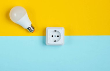 Beyaz plastik priz ve mavi sarı arka planda Led ampulü. Minimalizm. Üst görünüm