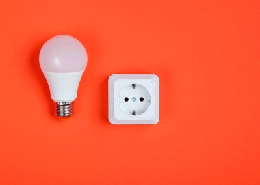 Beyaz plastik priz ve turuncu arka planda Led ampul. Minimalizm. Üst görünüm