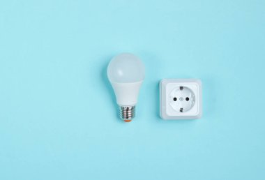 Beyaz plastik priz ve mavi arka planda Led ampul. Minimalizm. Üst görünüm