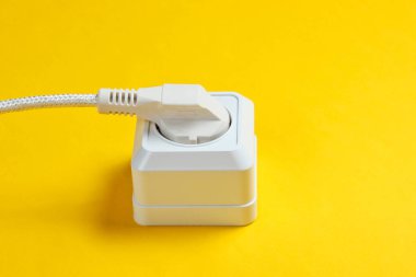 Sarı arkaplanda elektrik prizine bağlı beyaz kablo