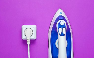 Mor arka planda elektrik prizine takılan şeyleri ütülemek için kablo demiri. Üst görünüm, minimalizm
