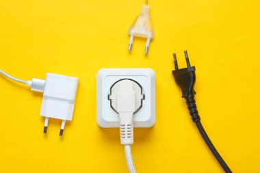 Elektrik bağımlılığı kavramı. Sarı arkaplanda elektrik prizlerinin yanında bir sürü elektrik prizi var.