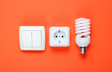 Ekonomik spiral ampul, elektrik prizi, turuncu arka plan düğmesi. Üst Manzara. Minimalizm elektro tüketici kavramı