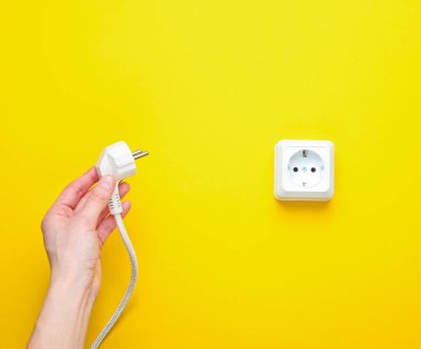 Dişi eller elektrik prizini sarı arkaplandaki elektro prize takıyor. Minimalizm. Üst görünüm