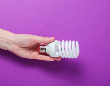 Mor arka planda spiral bir ampul tutan bir kadın el..