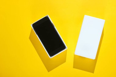 Sarı kağıttan arka planda açık bir kutuda yeni bir akıllı telefon. Üst görünüm, minimalizm