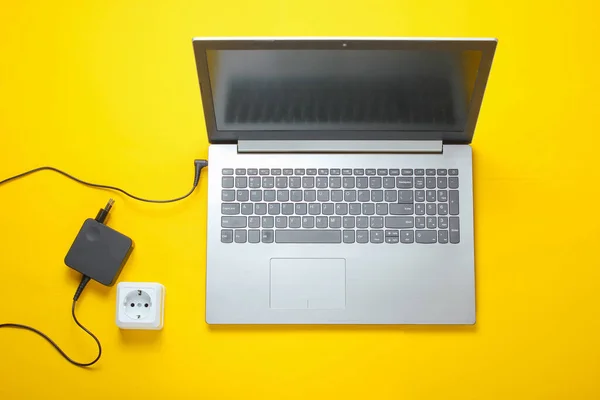 Female hand plugs a laptop charger into an electrical outlet on yellow background