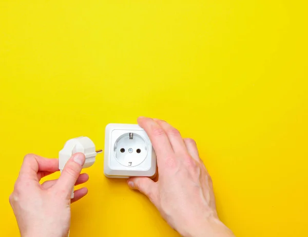 Female hands plug in power plug into electro outlet on yellow background. Minimalism. Top view