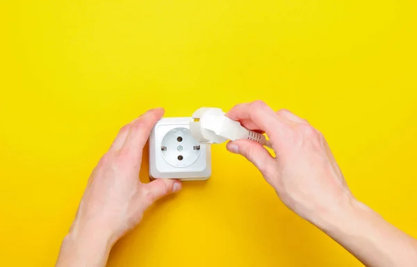 Female hands plug in power plug into electro outlet on yellow background. Minimalism. Top view